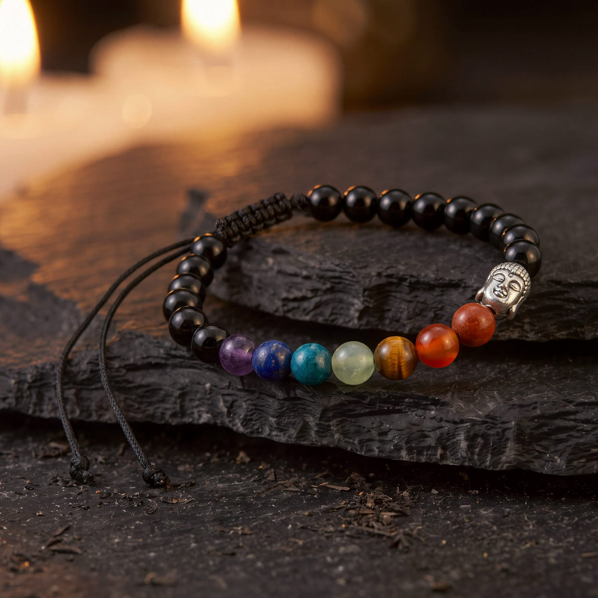 Pulsera 7 Chakras Ónix 6 mm con cabeza de Buda plateada sobre una piedra oscura, con velas al fondo