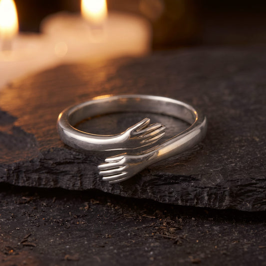 Anillo Abrazo Eterno en color plateado sobre una piedra oscura, con velas encendidas al fondo