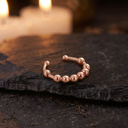 Anillo Calma giratorio en oro rosa sobre una piedra oscura, con velas encendidas al fondo