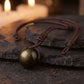 Collar Obsidiana Dorada con esfera de obsidiana y cordón café trenzado sobre una piedra oscura, con velas al fondo