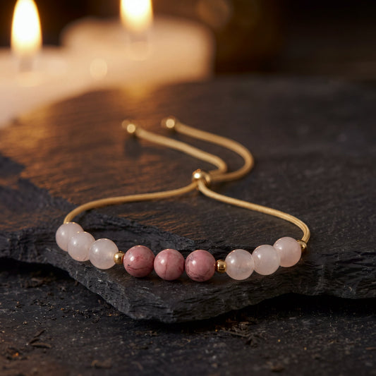 Pulsera Manifiesto de Amor con cuarzo rosa y rodonita sobre una piedra oscura, con velas encendidas al fondo