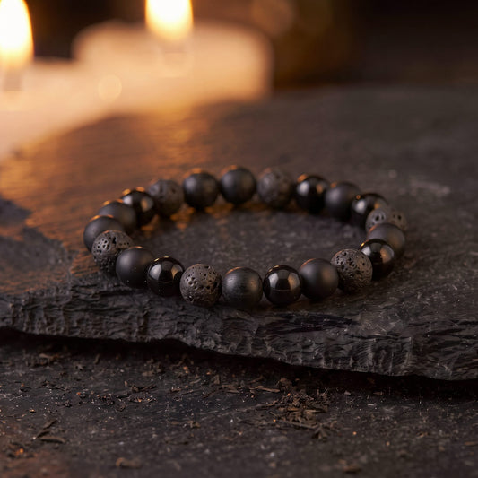 Brazalete Protección por 4 con obsidiana, ónix, piedra volcánica y turmalina sobre una piedra oscura, con velas al fondo
