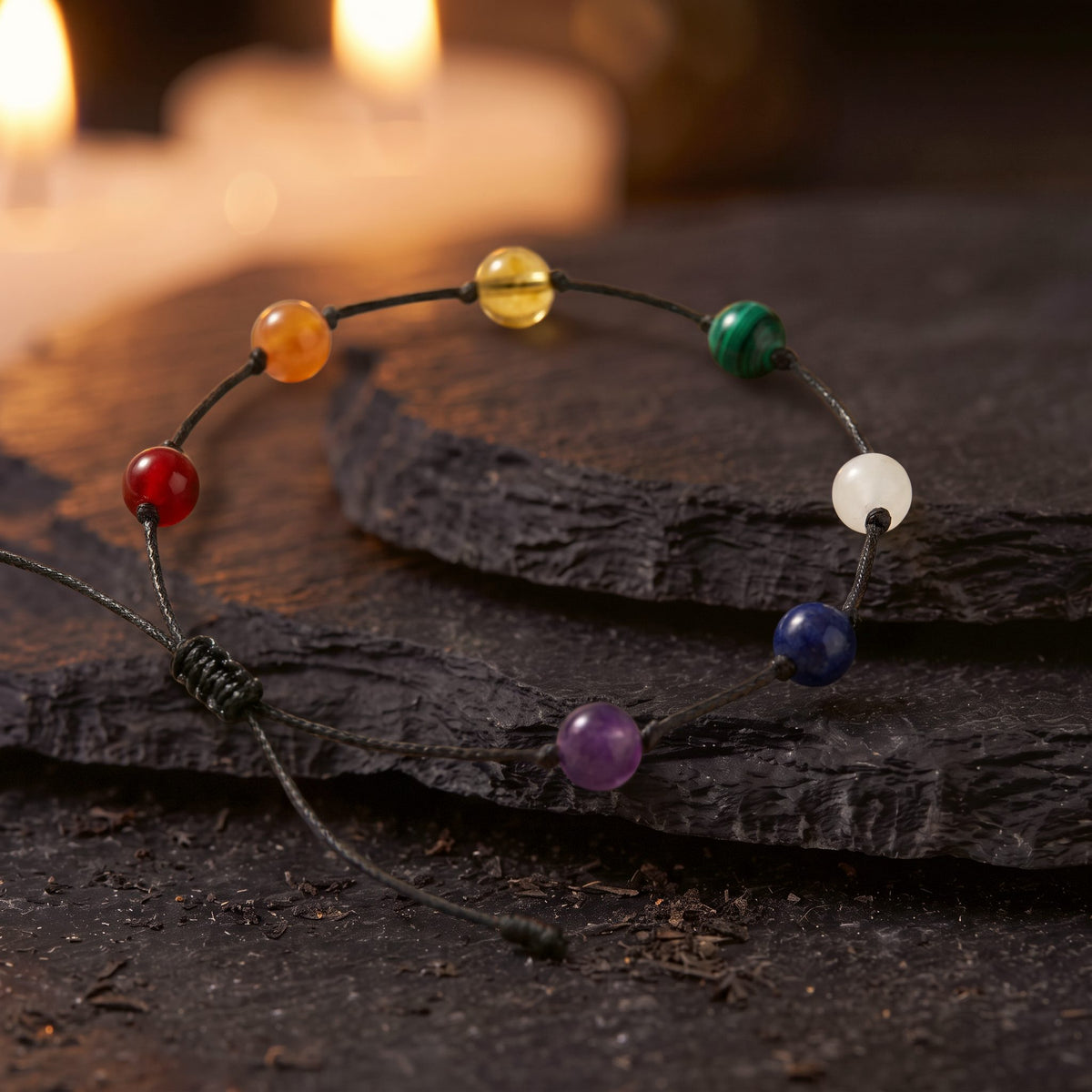 Tobillera 7 Chakras en cordón negro sobre una piedra oscura, con velas al fondo